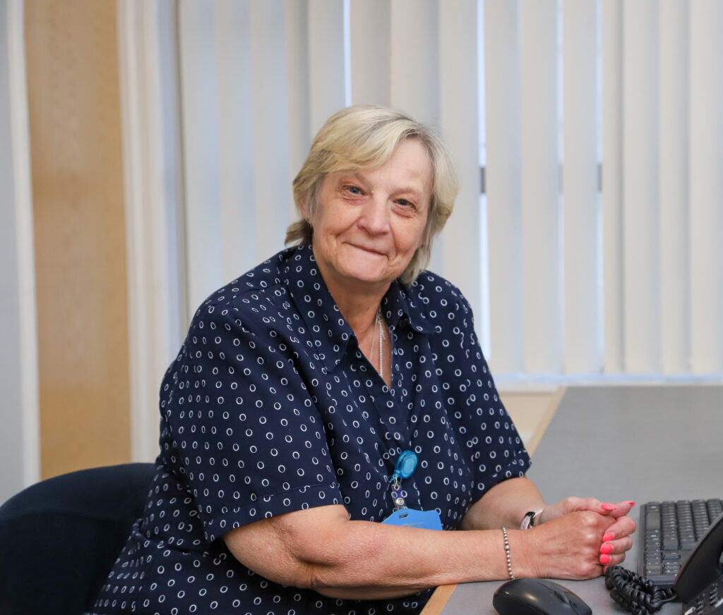 Ward Clerk Den Short sits at a computer with her arms resting on the desk